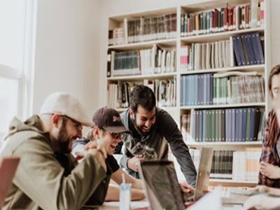 People looking at a laptop in front of a bookshelf